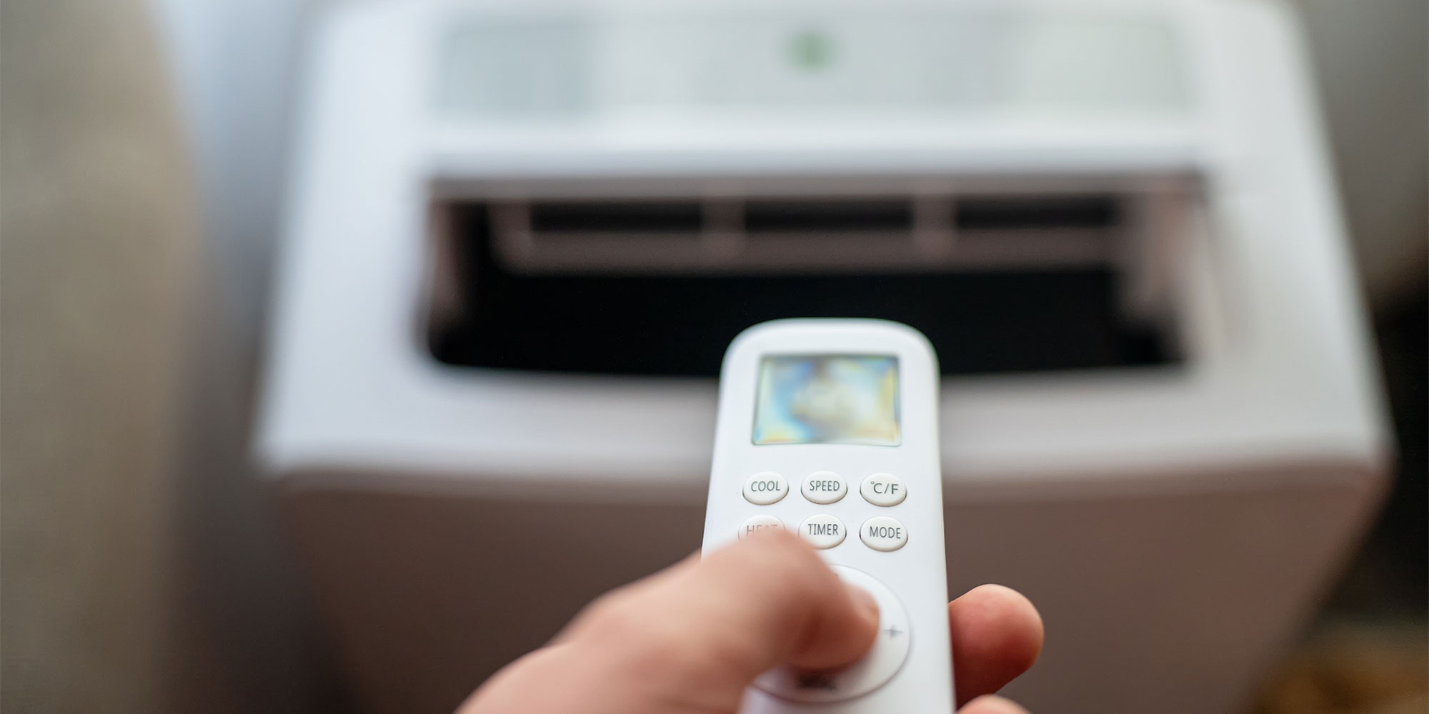 Remote control in foreground pointing at air conditioner in the background