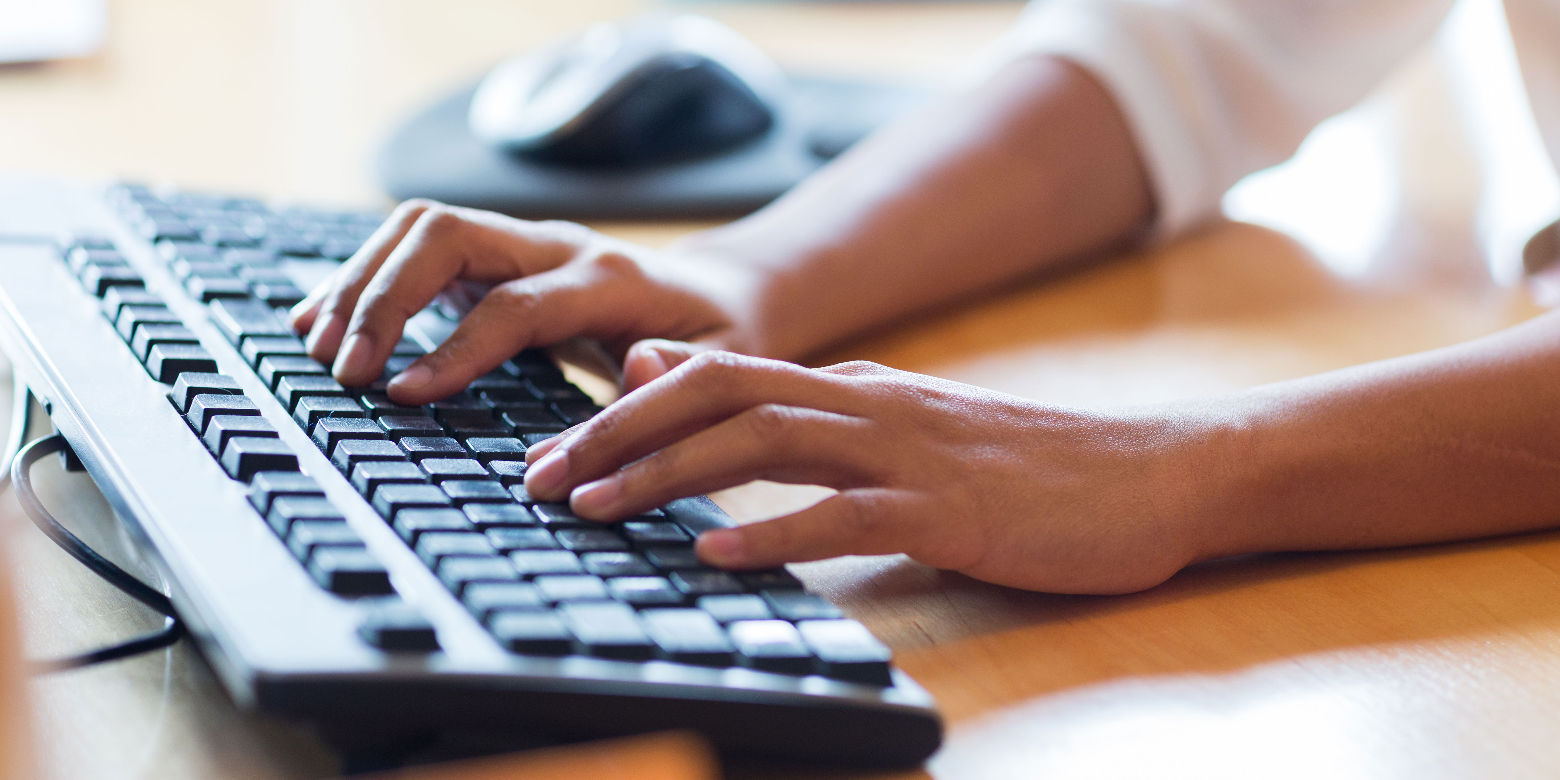 Two hands typing on a keyboard on a desk.