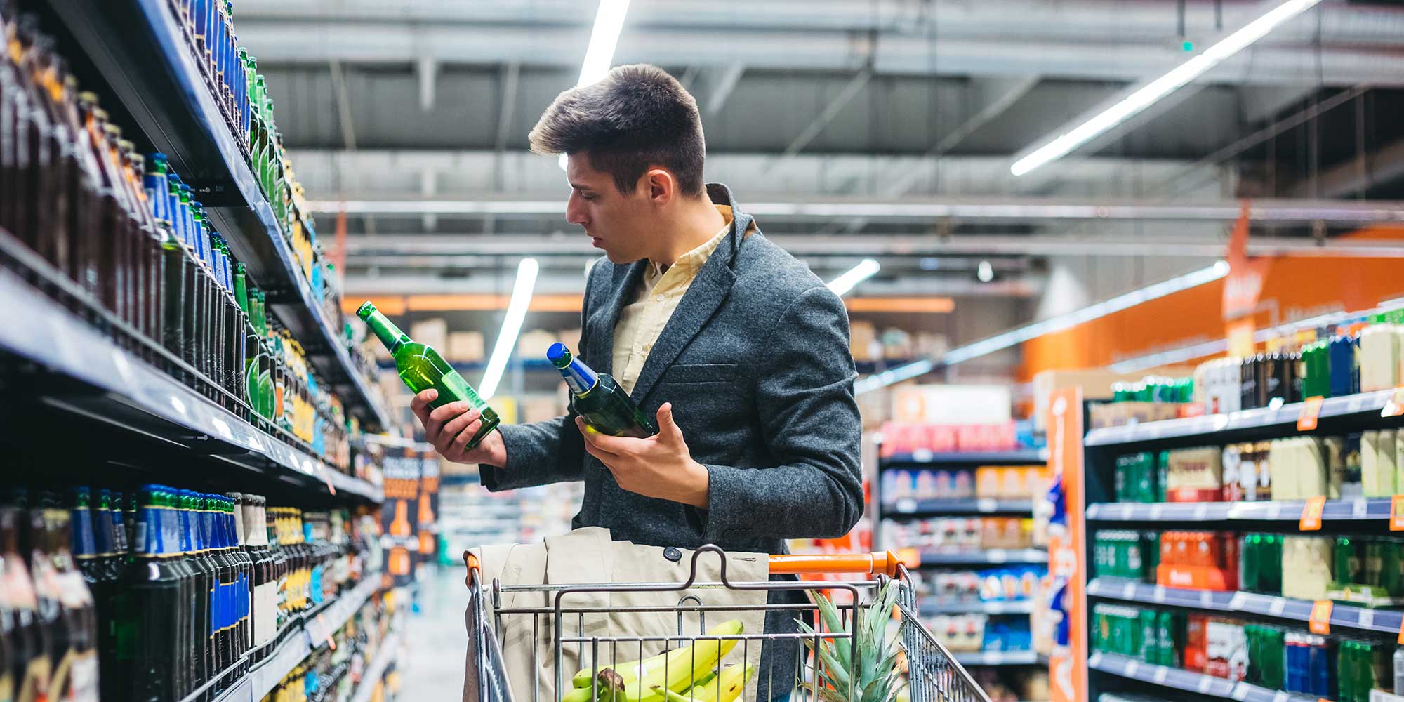 Man in supermarket looking at bottles of beer with a confused look