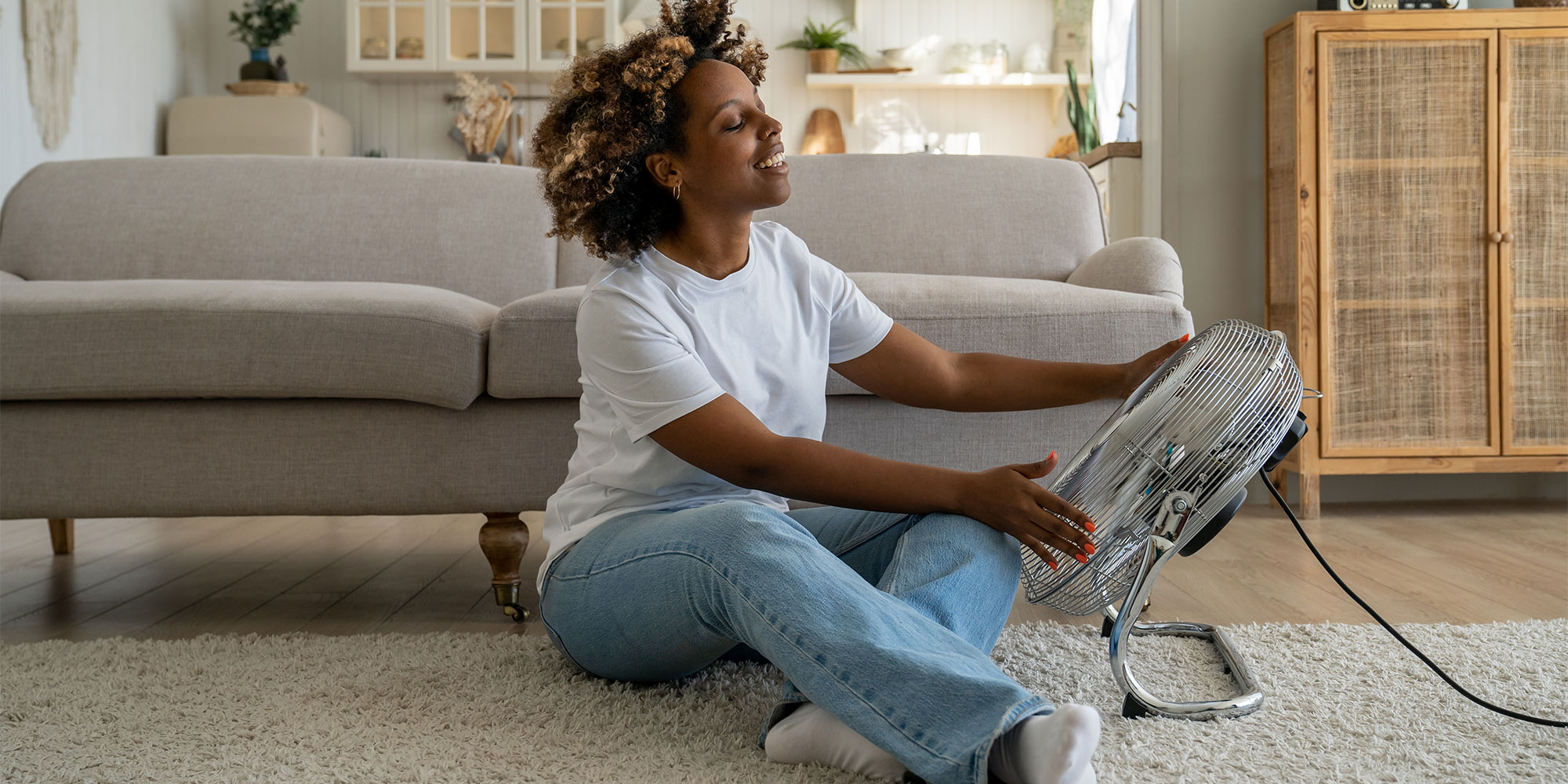 Woman sat on floor pointing large fan at themselves